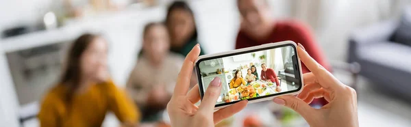 Woman taking photo of multicultural family and thanksgiving dinner at home, banner — Stock Photo