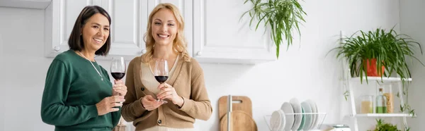 Cheerful interracial mom and daughter holding glasses of wine during thanksgiving celebration, banner — Stock Photo
