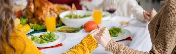 Обрізаний вид на сім'ю, що тримає руки біля вечері подяки з індичкою вдома, банер — стокове фото