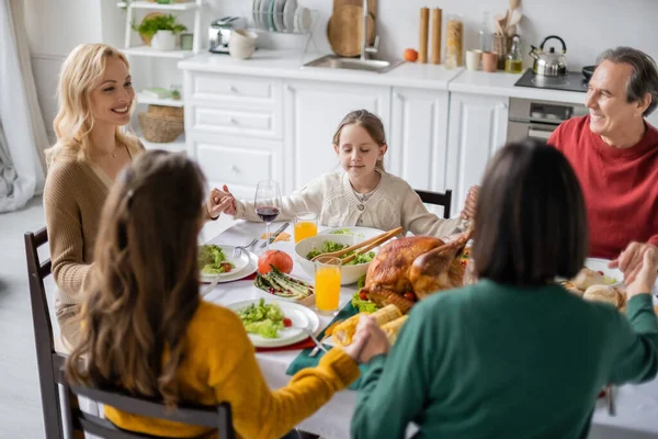 Familia sonriente tomados de la mano cerca de la cena de acción de gracias con bebidas en casa - foto de stock