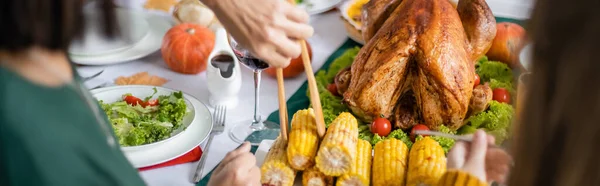 Vista recortada de la mujer tomando maíz cerca de nieto y pavo de acción de gracias en casa, pancarta - foto de stock