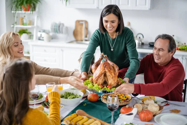 Sourire grand-parent multiethnique tenant la dinde près de la famille à la maison — Photo de stock