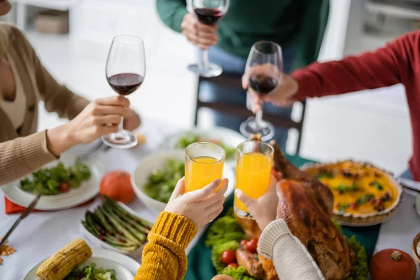 Vista recortada de los niños sosteniendo jugo de naranja cerca de los padres con vino y cena de acción de gracias en casa - foto de stock