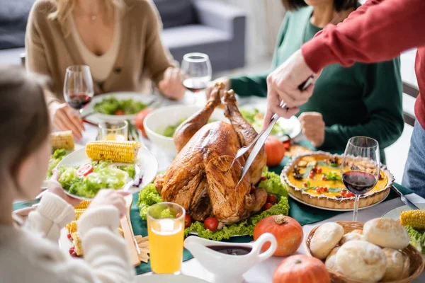 Avô cortando peru perto da família turva e criança celebrando ação de graças em casa — Fotografia de Stock