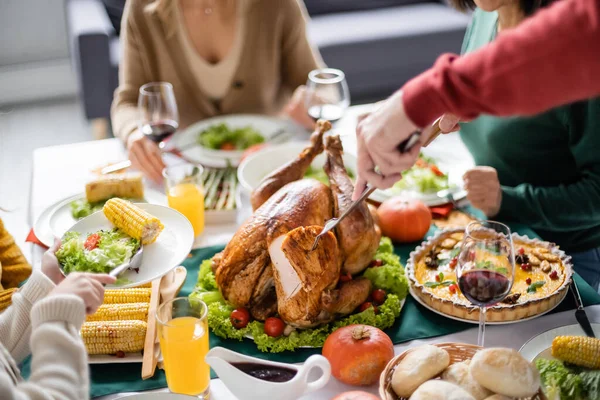 Cropped view of girl holding plate while grandparent cutting thanksgiving turkey at home — Stock Photo