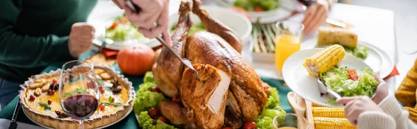 Partial view of girl holding plate near grandparent cutting thanksgiving turkey at home, banner — Stock Photo