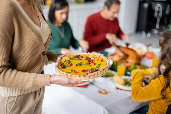 Woman holding thanksgiving pie near blurred family celebrating thanksgiving at home — Stock Photo
