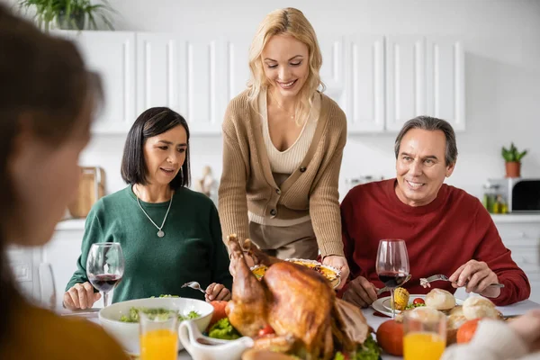 Mujer poniendo pastel cerca del pavo mientras celebra Acción de Gracias con la familia multiétnica en casa — Stock Photo