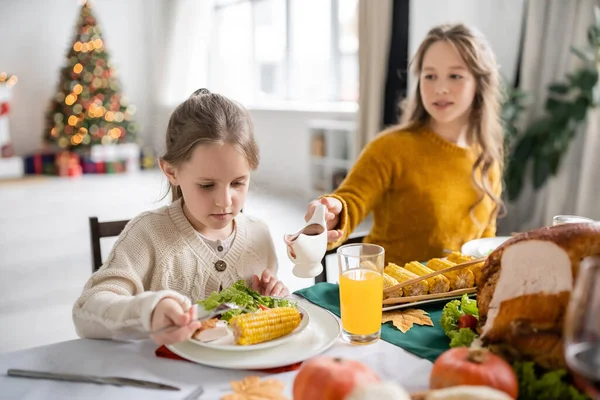 Ragazza guardando insalata e mais vicino sorella offuscata con salsa durante la cena del Ringraziamento a casa — Foto stock