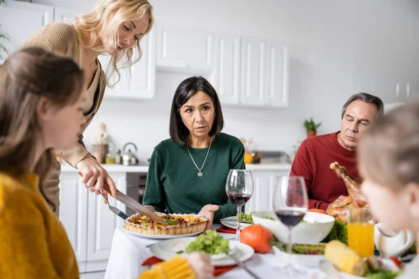 Многонациональная бабушка и дедушка разговаривают с размытыми детьми во время ужина в честь Дня Благодарения дома — стоковое фото