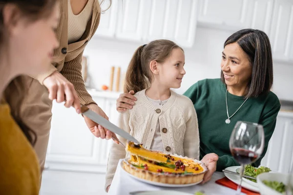 Sorridente nonna abbracciare bambino vicino cena del Ringraziamento con la famiglia a casa — Foto stock