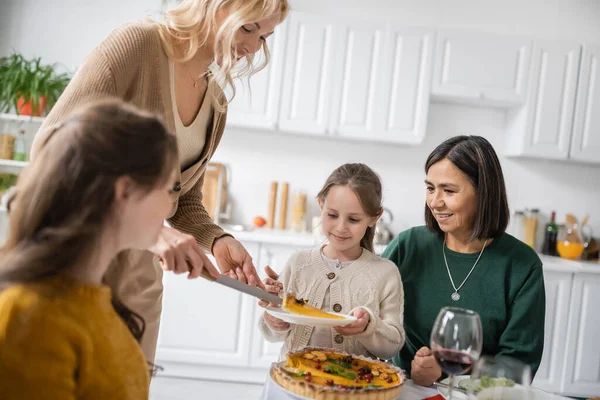 Mujer poniendo pastel de acción de gracias en el plato cerca de la familia interracial en casa - foto de stock