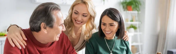 Cheerful woman hugging interracial parents during thanksgiving celebration at home, banner — Stock Photo