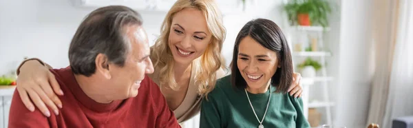 Mujer alegre abrazando a los padres interracial durante la celebración de Acción de Gracias en casa, pancarta - foto de stock