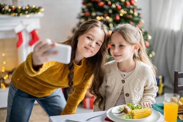 Smiling sisters taking selfie on smartphone during thanksgiving dinner at home — Stock Photo