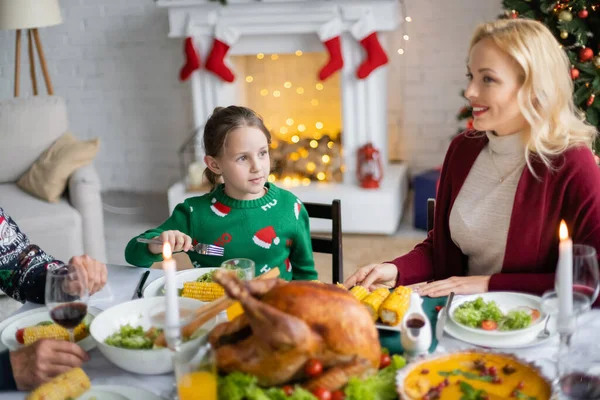 Girl holding fork during christmas dinner with mom and grandfather in living room with decorated fireplace — Stock Photo