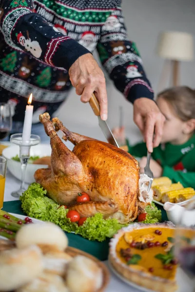 Partial view of senior man cutting traditional thanksgiving turkey near blurred granddaughter — Stock Photo