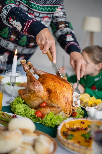 Vista parcial del hombre mayor cortando pavo tradicional de acción de gracias cerca de nieta borrosa - foto de stock