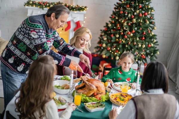 Mann schneidet leckeren Truthahn in der Nähe lächelnder Familie beim festlichen Weihnachtsessen — Stockfoto