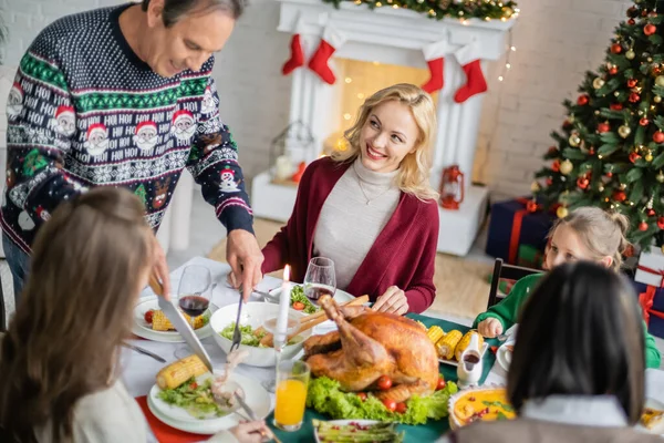 Улыбающийся пожилой человек, подающий жареную кукурузу рядом с размытой внучкой во время празднования Рождества — стоковое фото