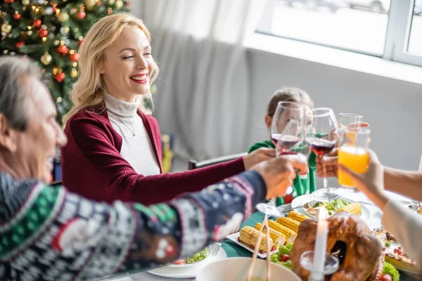 Feliz familia tintineo vasos con vino tinto y jugo de naranja mientras se celebra la Navidad en casa - foto de stock
