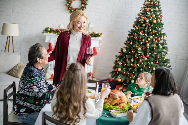 Femme souriante griller avec un verre de vin rouge pendant le dîner de Noël avec la famille interracial — Photo de stock