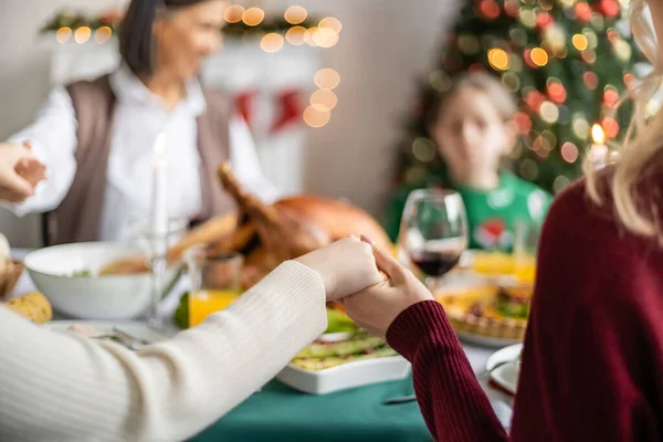 Multiethnic family holding hands and praying before christmas dinner on blurred background — Stock Photo