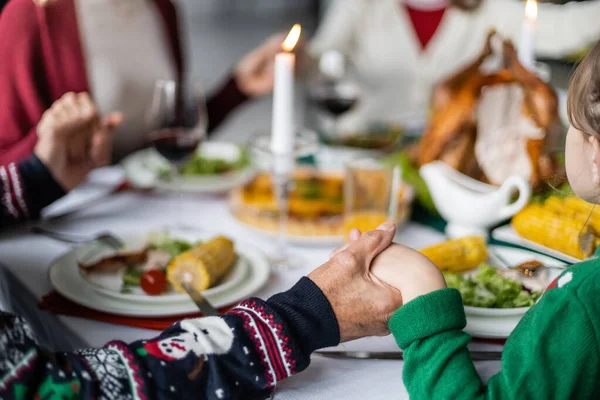 Partial view of family holding hands during pray before thanksgiving dinner on blurred background — Stock Photo