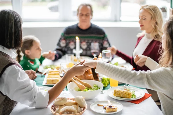 Famille interracial avec les yeux fermés tenant la main et priant avant le dîner de Thanksgiving — Photo de stock