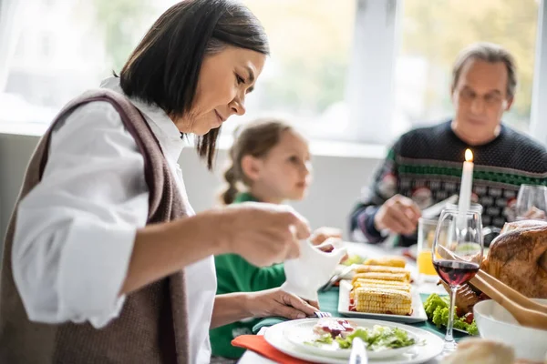 Femme multiraciale tenant le bateau de sauce pendant le dîner festif de thanksgiving avec la famille — Photo de stock