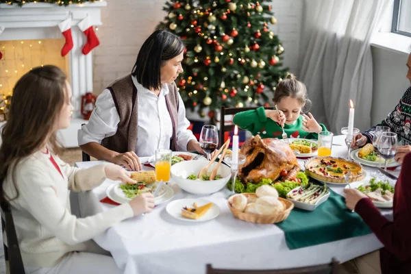 Multiracial woman looking at granddaughter during christmas dinner with family — Stock Photo