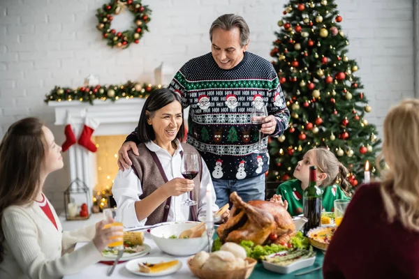 Sorridente donna multirazziale brindare con un bicchiere di vino rosso durante la cena di Natale con la famiglia — Foto stock