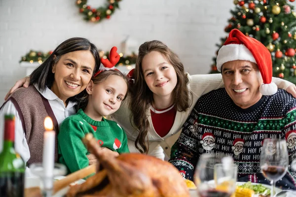 Abuelos interracial y nietas sonriendo a la cámara cerca de deliciosa cena de Navidad en primer plano borrosa - foto de stock