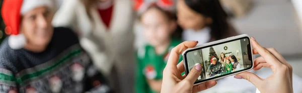 Mulher com telefone celular tirando foto de família multiétnica durante a celebração do Natal, banner — Fotografia de Stock