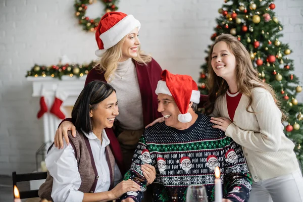 Cheerful teenage girl smiling near mother and interracial grandparents in living room with christmas decoration — Stock Photo