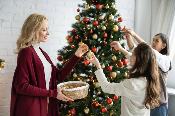 Menina adolescente com mãe e avó multirracial decorando árvore de Natal na sala de estar — Fotografia de Stock