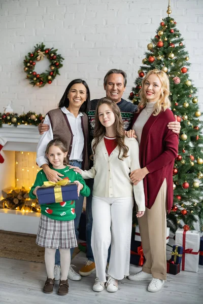 Heureuse famille multiethnique souriant à la caméra dans le salon avec cheminée et arbre de Noël décoré — Photo de stock