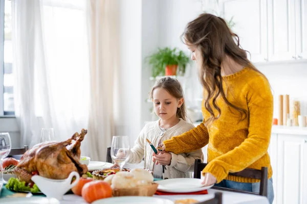 Sorelle che tengono posate mentre servono tavola con cena festiva del Ringraziamento in cucina — Foto stock