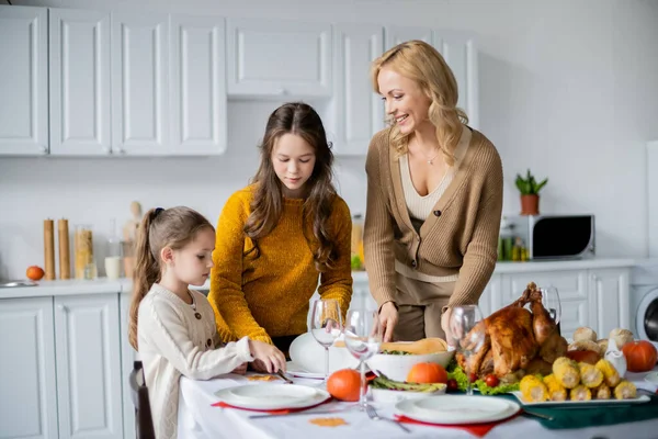 Girls with happy mother serving thanksgiving dinner near roasted turkey and grilled corn — Stock Photo