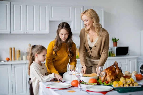 Mädchen mit glücklicher Mutter servieren Erntedankdinner in der Nähe von gebratenem Truthahn und gegrilltem Mais — Stockfoto