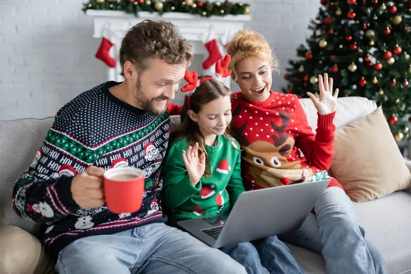 Smiling family in christmas sweaters having video call on laptop at home — Stock Photo
