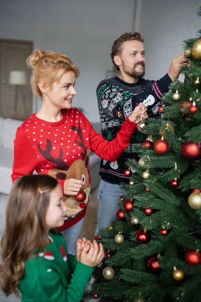Positive woman in sweater decorating christmas tree with family at home — Stock Photo