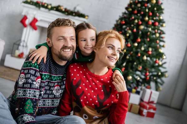 Smiling girl hugging parents in christmas sweaters at home — Stock Photo
