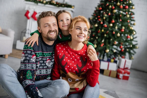 Positive girl hugging parents in christmas sweaters at home — Stock Photo