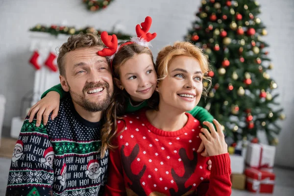 Cheerful kid in christmas headband hugging family at home — Stock Photo