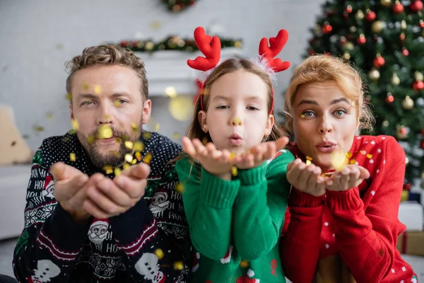 Famille en chandails chauds soufflant confettis pendant Noël à la maison — Photo de stock