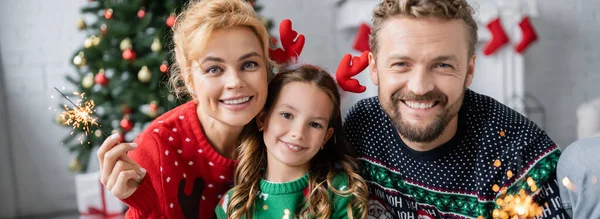 Glückliche Familie mit Kind hält Wunderkerzen während der Weihnachtsfeier zu Hause, Banner — Stockfoto