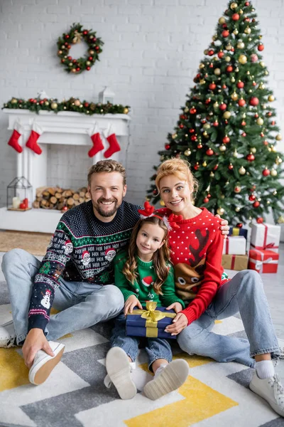 Família positiva segurando presente de Natal perto de decoração festiva em casa — Fotografia de Stock