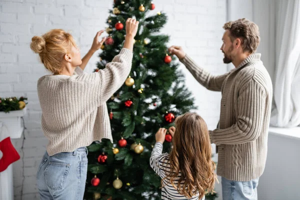 Family decorating christmas tree with festive baubles at home — Stock Photo