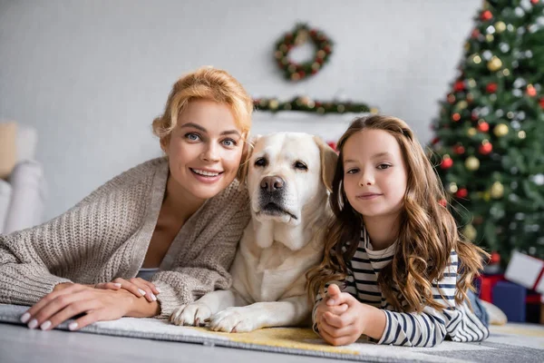 Madre e figlio positivo guardando la fotocamera vicino labrador a casa — Foto stock